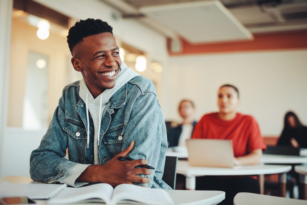 Un étudiant assis dans une salle de classe à l'université regarde au loin et sourit.