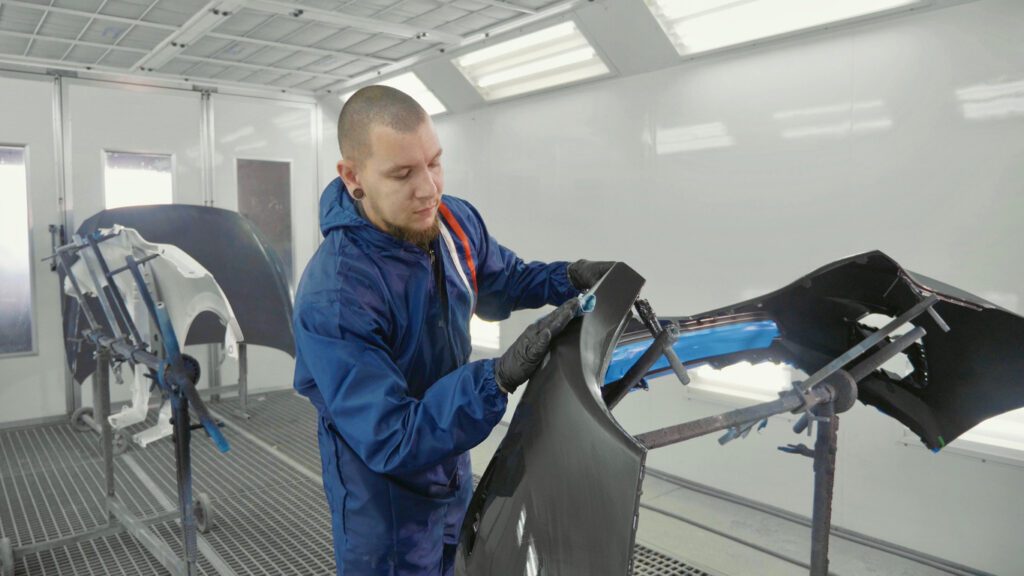Étudiant du DEP en carrosserie automobile au CFP de Verdun préparant une pièce de carrosserie dans une cabine de peinture professionnelle.